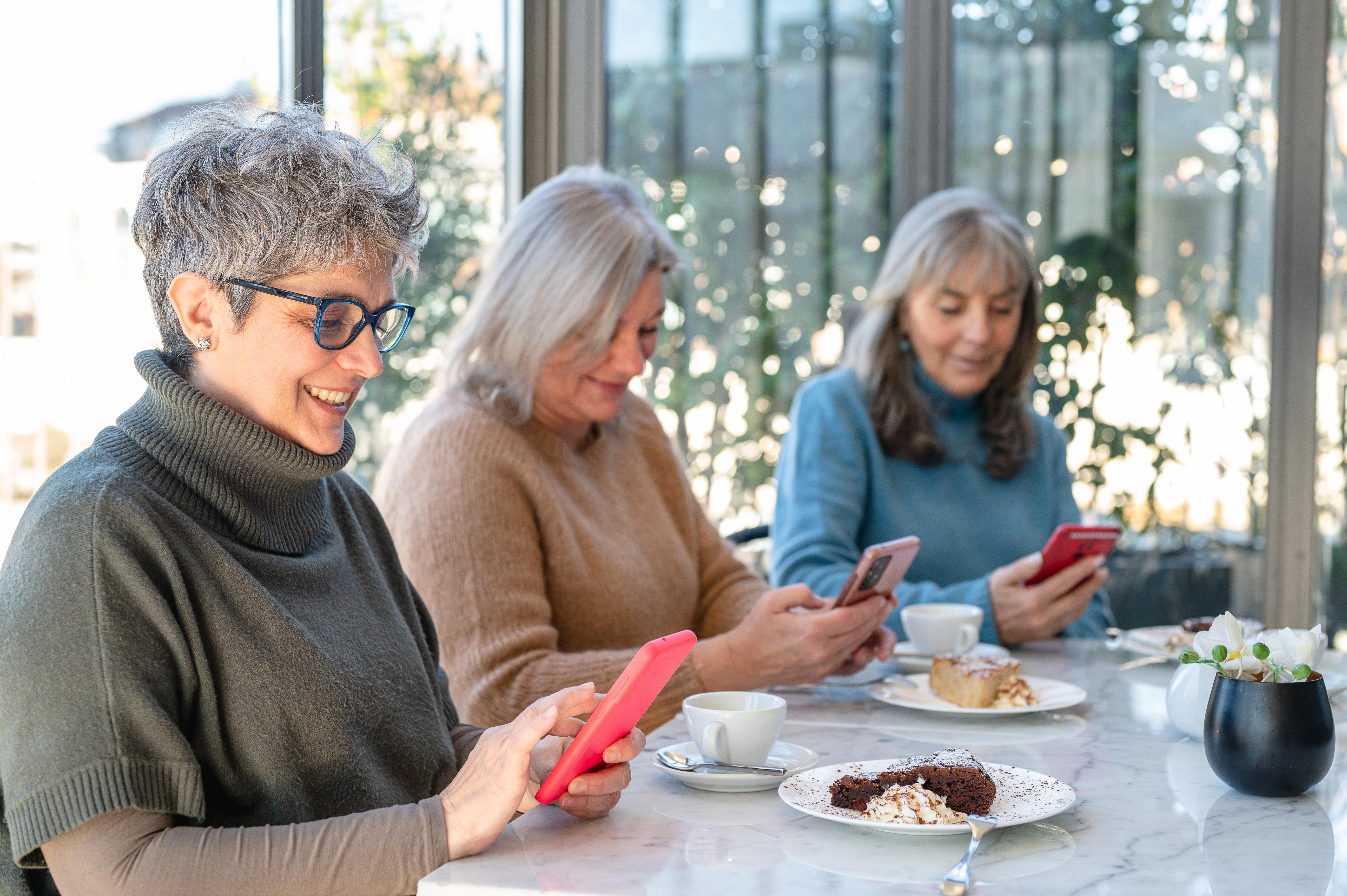 Three women sat together booking courses on their smart phones