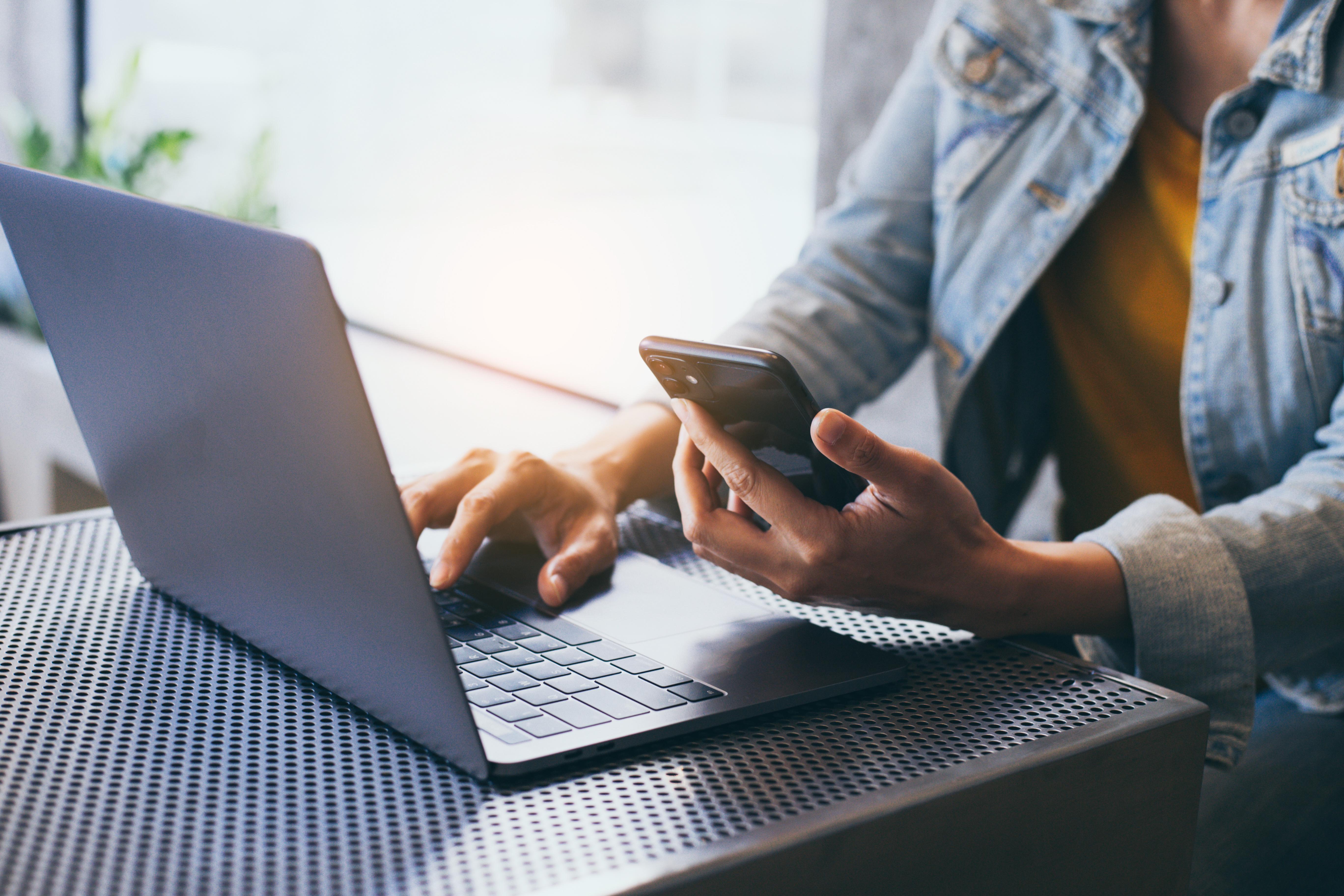 A woman's hands using a phone and laptop