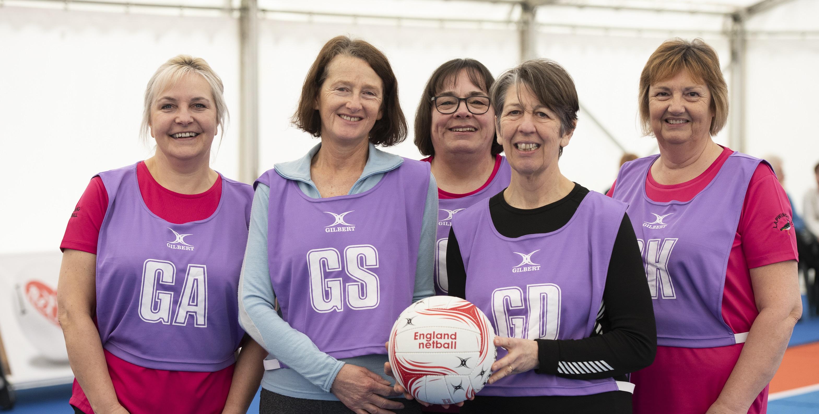 WI members stood together smiling, wearing netball jerseys and holding a netball
